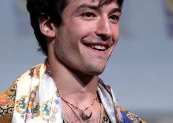 Ezra Miller wearing a white scarf and multi-colored shirt