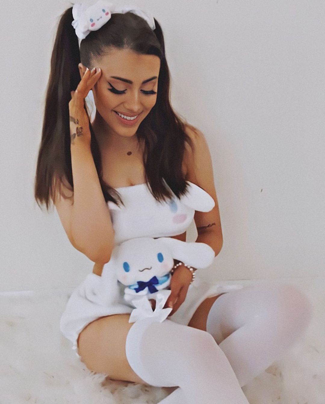 Paige Niemann wearing a white dress holding a soft toy